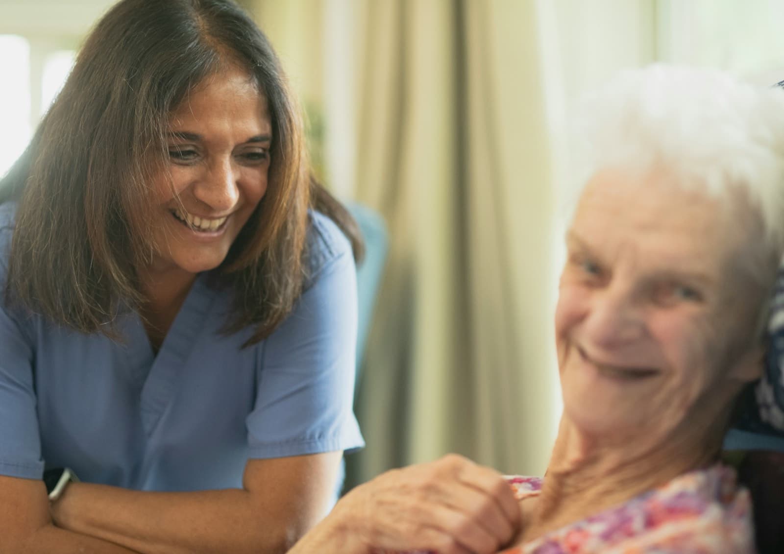 A smiling caregiver sitting with an elderly woman