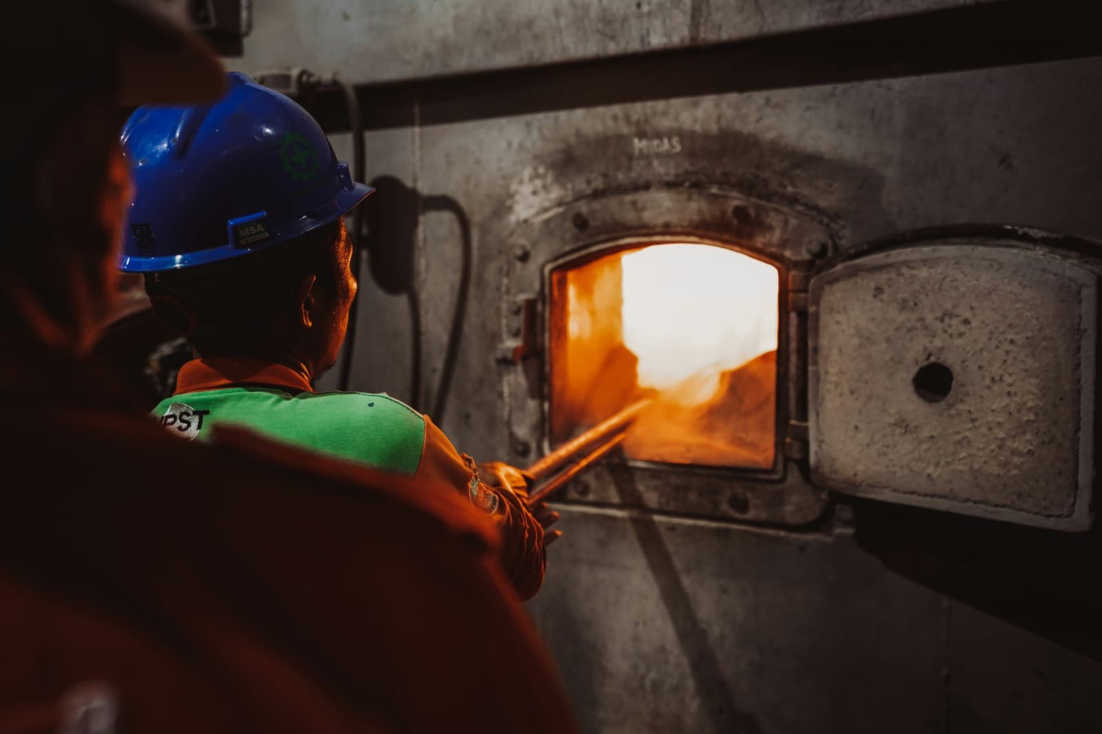 A technician in a hard hat working at an open furnace