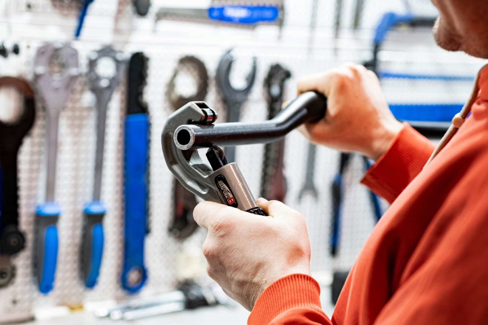 A plumber holding a pipe wrench in front of a wall of tools