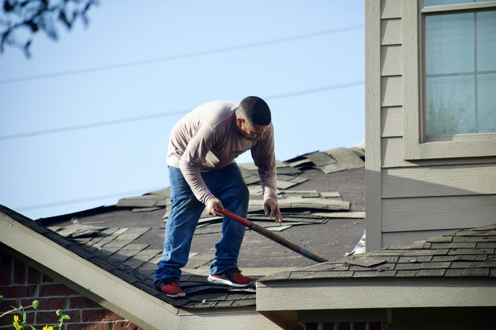 A roofer removing old shingles from a house